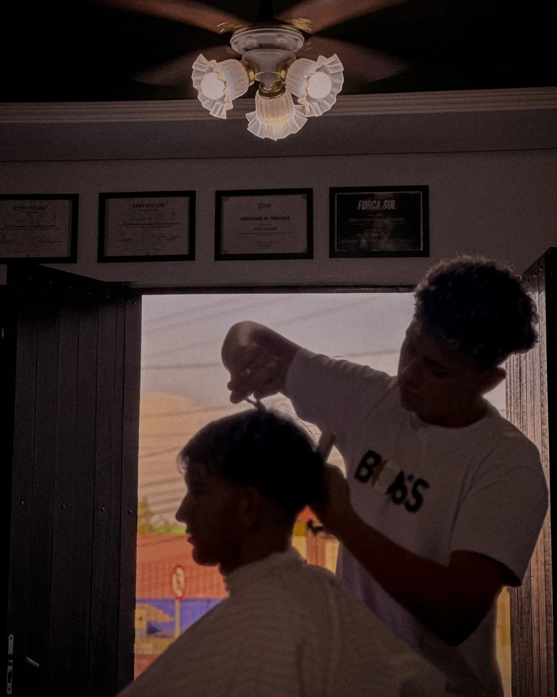 Barbeiro da Punchline cortando o cabelo de um cliente, com os certificados emoldurados na parede ao fundo